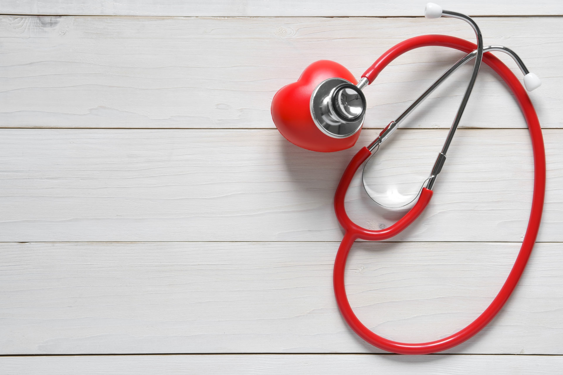 closeup red heart check with stethoscope medical instrument on top view white wood table for love or take care and treat heart disease for strength of health with space