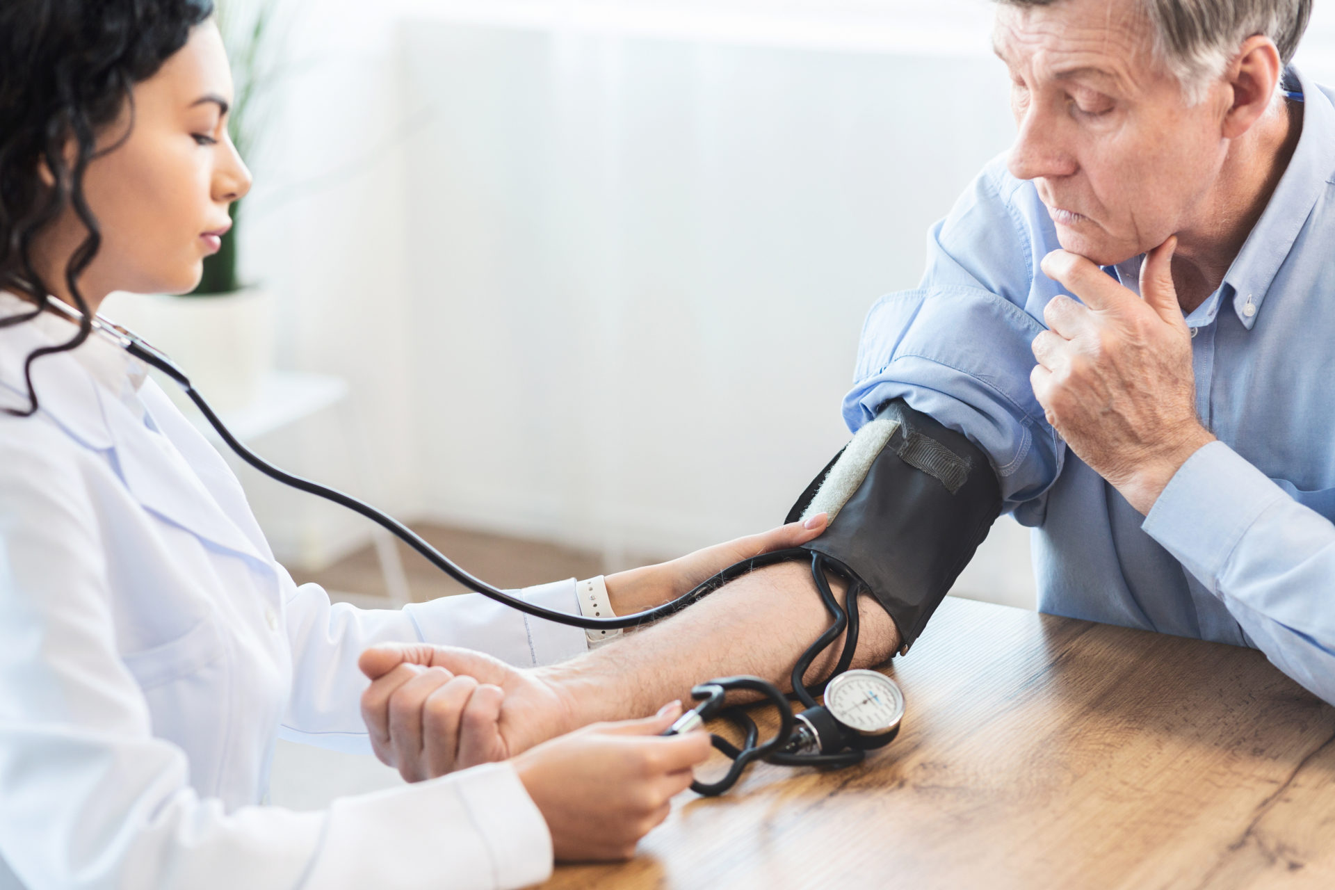 Cardiology. Mexican doctor measuring blood pressure of senior man, checking patient, free space